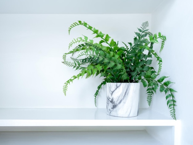 Vaso de cerâmica moderno branco com planta artificial com folhas verdes na prateleira branca com espaço de cópia