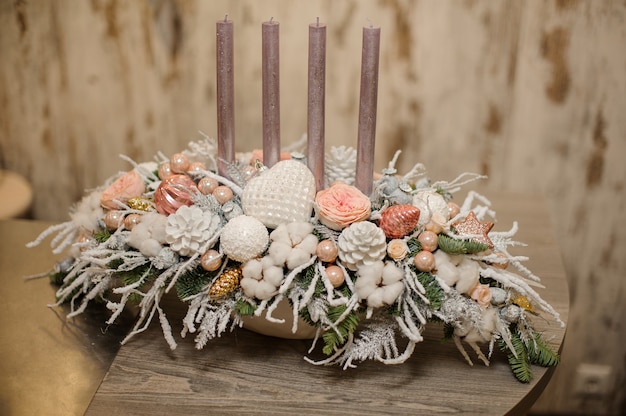 Foto vaso de cor branca com uma composição de decoração de natal de galhos de pinheiro, velas, flores e enfeites na mesa