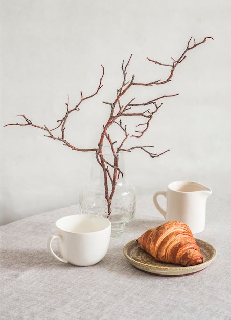 Vaso de croissant interior para casa escandinavo com jarro de leite de ramos e copo sobre a mesa em uma sala aconchegante e brilhante