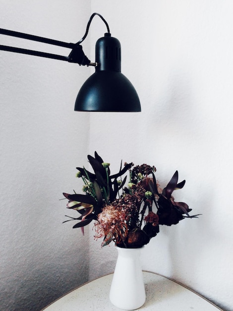 Foto vaso de flores abaixo da lâmpada elétrica contra a parede