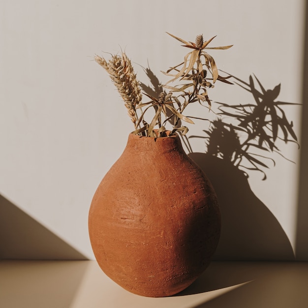 Vaso de flores de argila vermelha artesanal com buquê de centeio de trigo seco nas sombras do sol