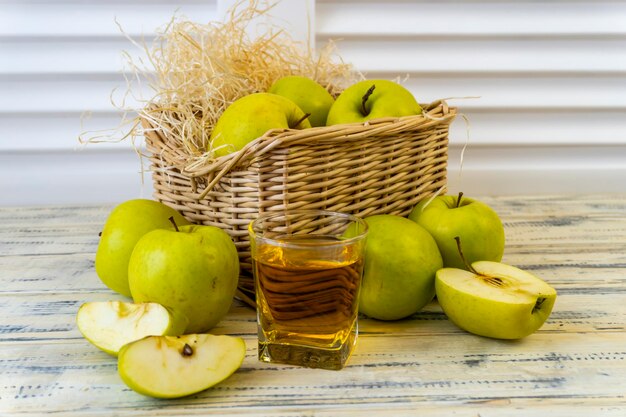 Vaso de maçãs verdes com suco de maçã e cesto com maçãs em fundo de madeira