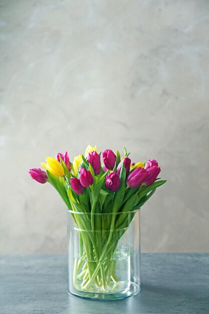 Vaso de vidro com buquê de lindas tulipas na cor de fundo