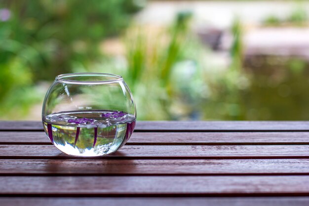 Vaso de vidro redondo com flores flutuantes na mesa de madeira com fundo desfocado