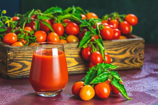 Vaso de delicioso jugo de tomate rojo jugoso fresco y tomates frescos en caja de madera Fondo oscuro Primer plano Libre de OGM Buena comida natural