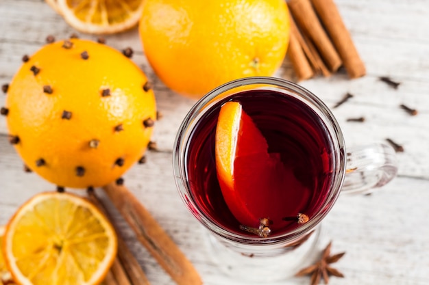 Vaso de delicioso vino caliente con naranja, anís, canela en la mesa de madera blanca