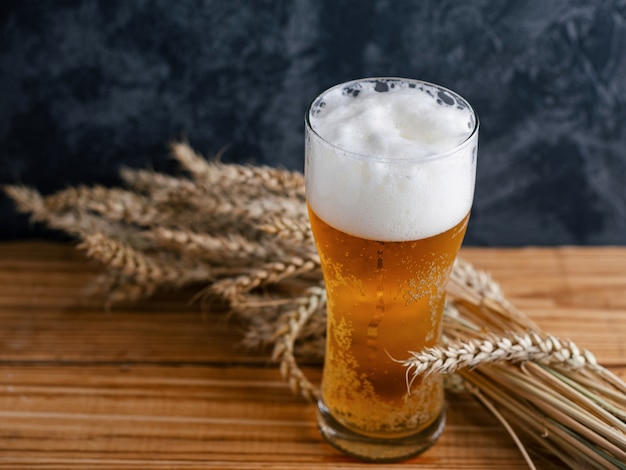 Vaso empañado de cerveza ligera en una mesa de madera y trigo