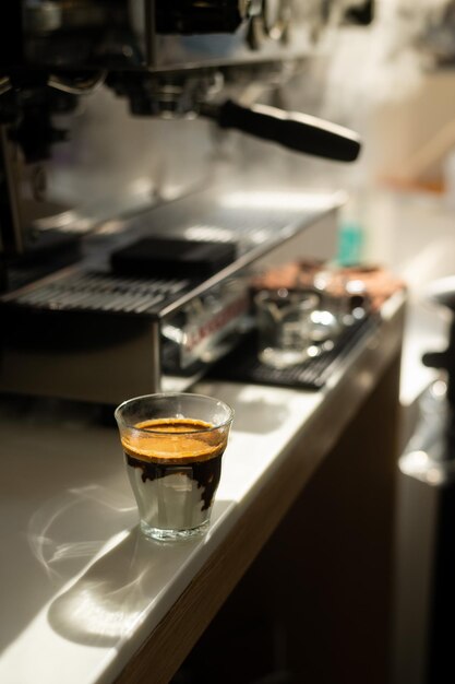 Un vaso de espresso se encuentra en un mostrador al lado de una máquina de café.