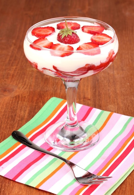 Vaso de fresas maduras con crema sobre fondo de madera