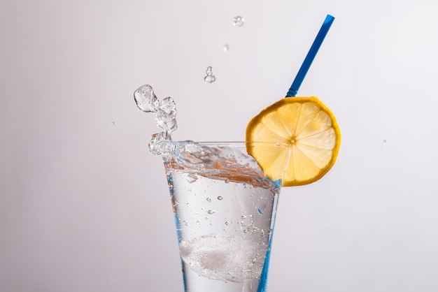 Vaso de gin tonic fresco con una rodaja de limón y una pajita sobre un fondo gris