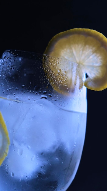 Vaso de gin tonic con hielo y limón sobre un fondo negro