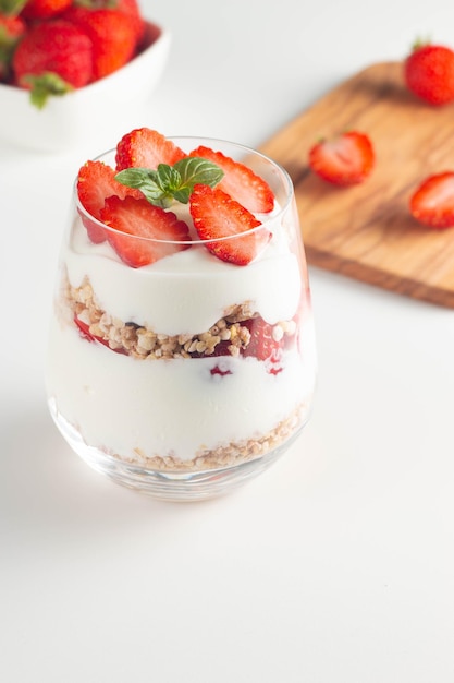 Vaso con granola, yogur y fresas frescas en el cuadro blanco. Concepto de tazón de desayuno saludable.