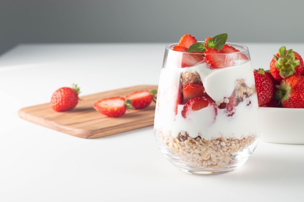 Vaso con granola, yogur y fresas frescas en el cuadro blanco. Concepto de tazón de desayuno saludable.