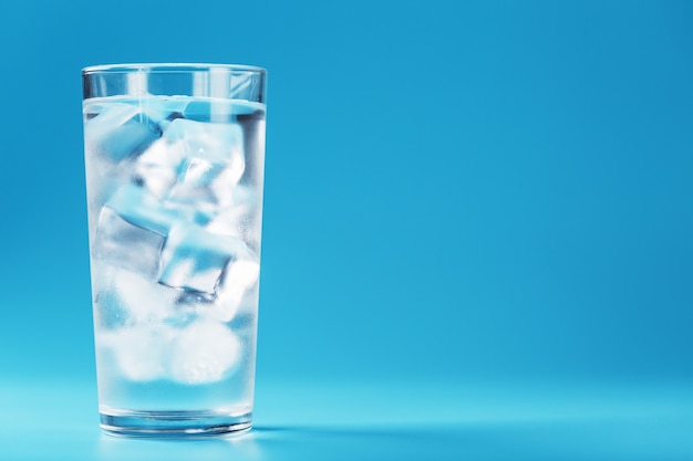 Un vaso con hielo y agua limpia sobre una superficie azul