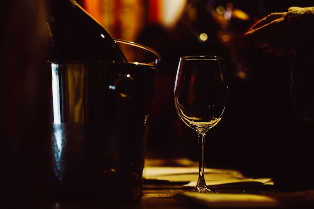 El vaso iluminado está en la mesa junto a las botellas de vino en un cubo para enfriar. Clave baja