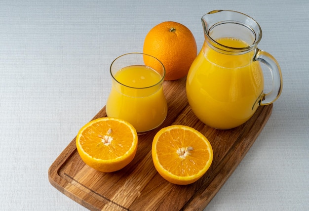 Vaso y jarra de jugo de naranja sobre un soporte de madera en rodajas de fondo de lino naranja