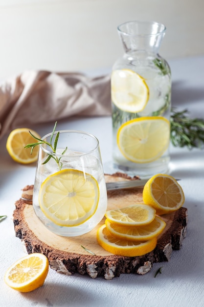 Un vaso y una jarra de limonada Rodajas de limón con hojas de romero en una bebida