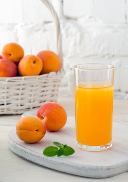 Vaso de jugo de albaricoque fresco y albaricoques maduros en canasta blanca sobre fondo de pared de ladrillo blanco. Enfoque selectivo. De cerca.