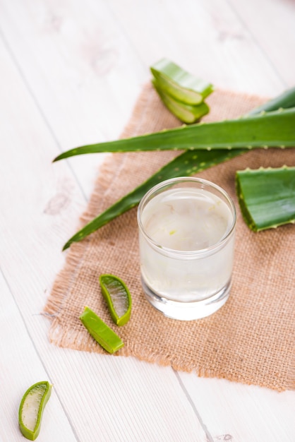 Vaso de jugo de aloe vera con hojas frescas sobre una mesa de madera