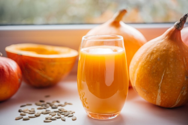 Un vaso de jugo de calabaza con semillas de calabaca en el alféizar de la ventana