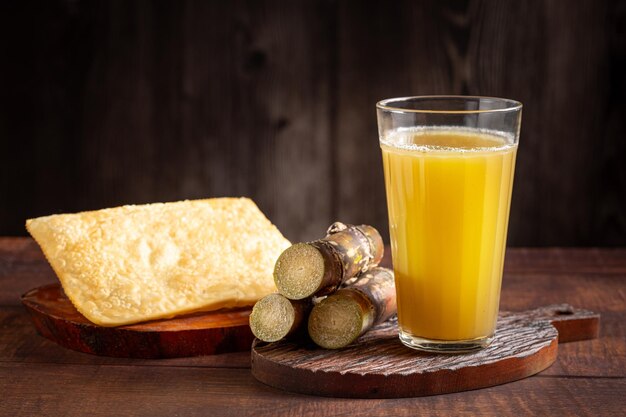 Vaso de jugo de caña de azúcar con pasteles fritos bocadillo típico brasileño