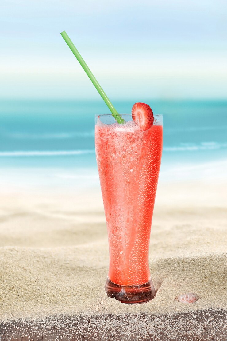 Vaso con jugo de fresa en la arena de la playa
