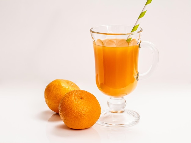 Vaso de jugo de fruta con paja y mandarinas frescas sobre fondo blanco.