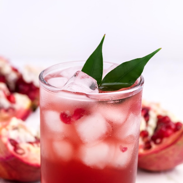 Vaso de jugo de granada con hielo y frutas frescas de granada en bebida de desintoxicación de fondo blanco