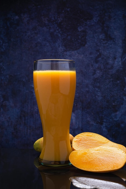 Vaso de jugo de mango y grupo de mangos en una mesa de vidrio negro. Fondo azul. Vista superior.