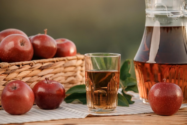 Un vaso con jugo de manzana y una canasta con manzanas sobre una mesa de madera con fondo de huerta natural Composición de frutas vegetarianas