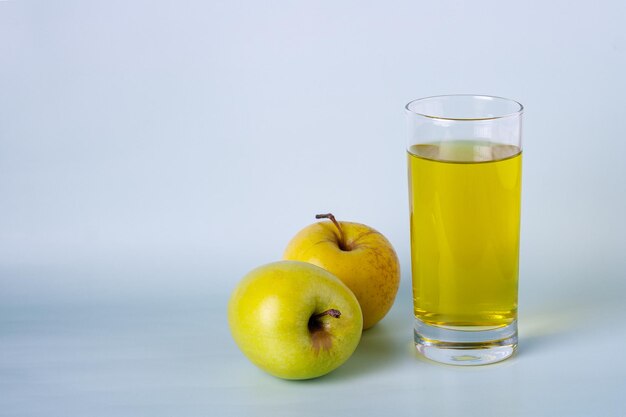 Un vaso de jugo de manzana y dos manzanas en un espacio de copia de fondo azul