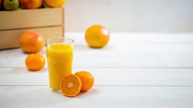 Vaso de jugo con naranja cortada en un escritorio blanco con espacio de copia