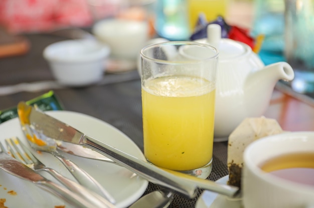 Un vaso de jugo de naranja está sobre una mesa con un plato y un tenedor.