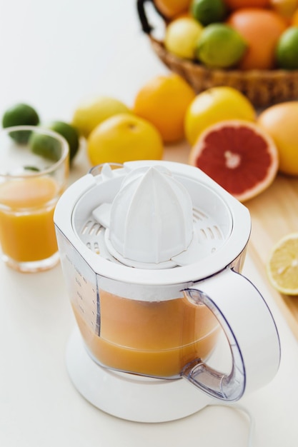 Vaso de jugo de naranja exprimidor de cítricos y varios cítricos en la mesa de la cocina