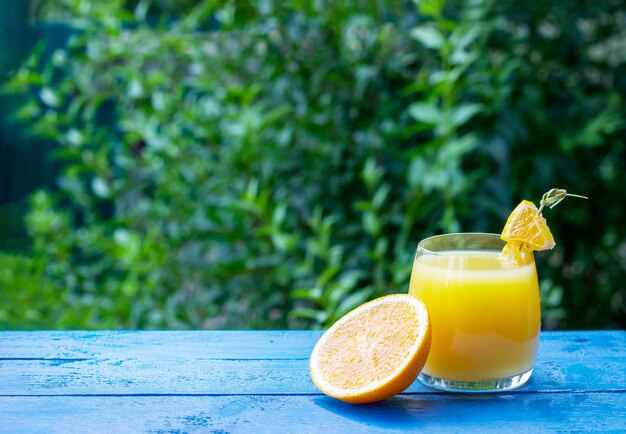 Vaso de jugo de naranja fresco adornado con una rodaja de naranja madura en la mesa de madera azul