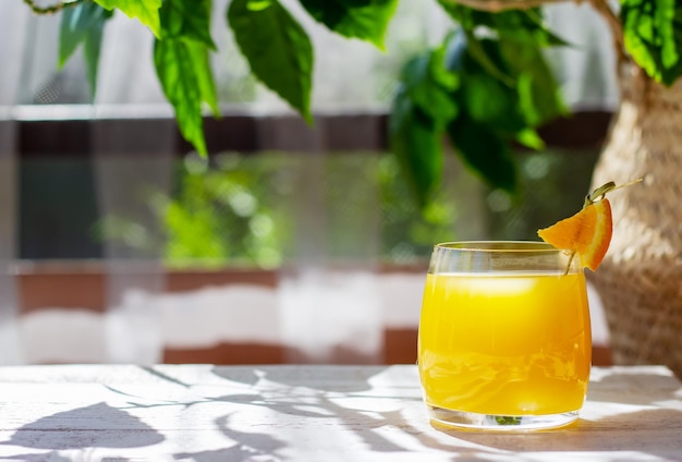 Vaso de jugo de naranja fresco adornado con una rodaja de naranja en la mesa de madera blanca en la terraza de verano