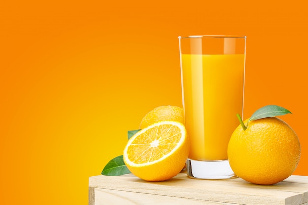 Vaso de jugo de naranja fresco en caja de madera, frutas frescas Jugo de naranja en vidrio con grupo sobre fondo de color naranja con copia Espacio para el texto.