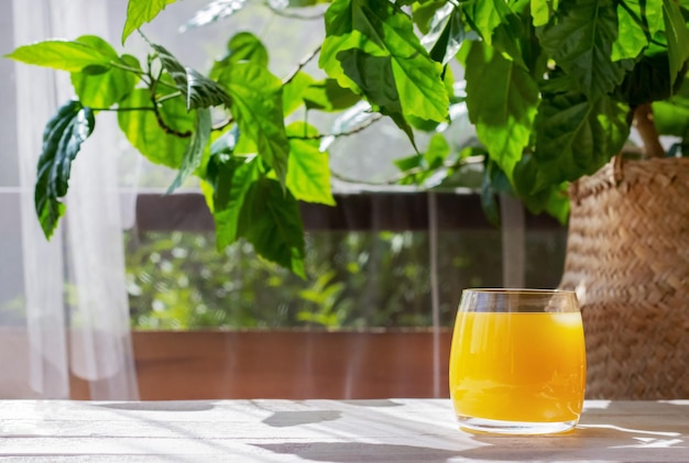 Vaso de jugo de naranja fresco en la mesa de madera blanca en la terraza de verano