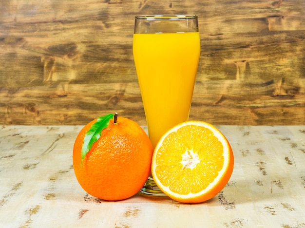 Un vaso de jugo de naranja fresco y naranjas sobre fondo de madera