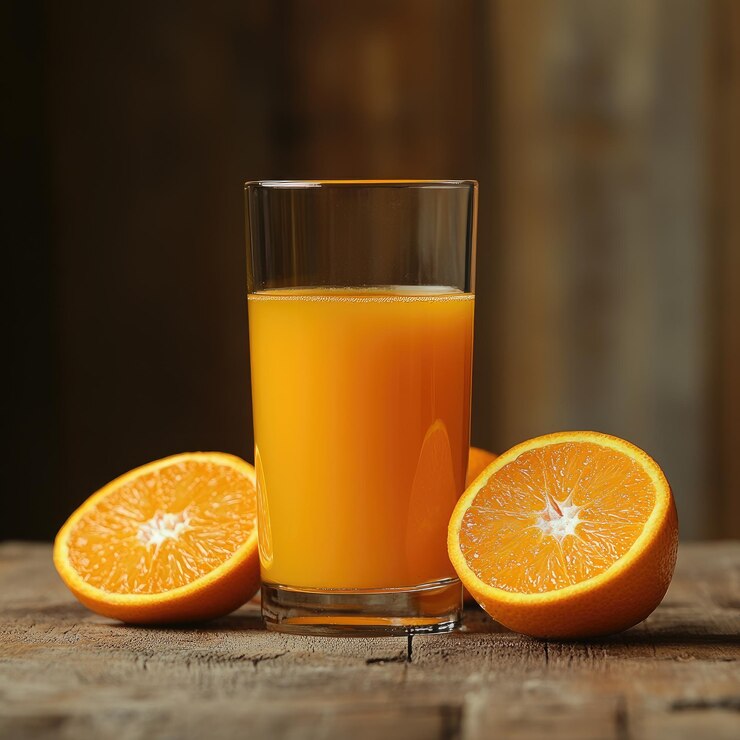 un vaso de jugo de naranja junto a dos naranjas