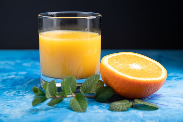 Vaso de jugo de naranja con menta sobre un fondo negro y azul. Vista lateral, de cerca.