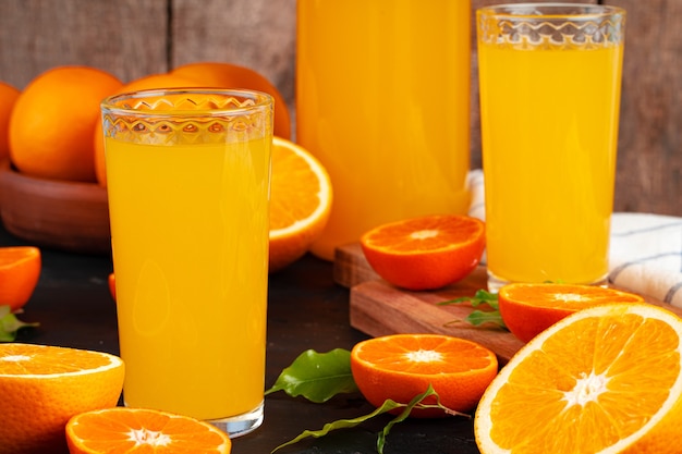 Vaso de jugo de naranja y naranjas cortadas en la mesa