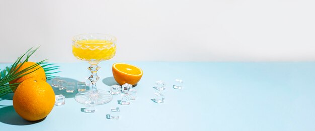 Vaso con jugo de naranja, naranjas, cubitos de hielo, hoja de palma