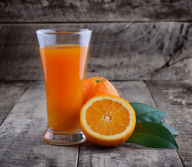 Vaso de jugo de naranja y naranjas frescas en madera