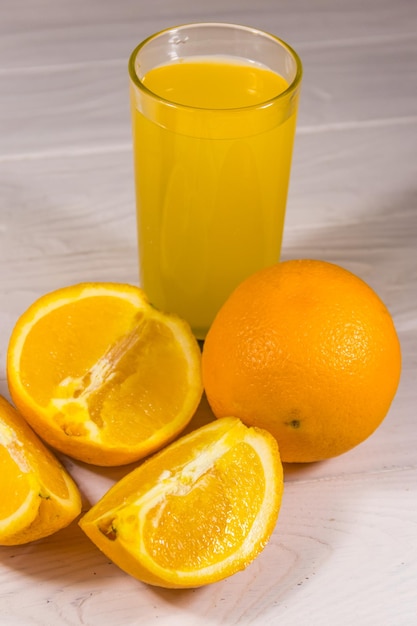 Vaso de jugo de naranja y naranjas frescas en la mesa de madera blanca