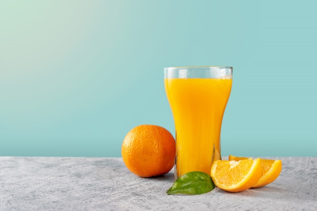 Vaso de jugo de naranja con naranjas en pared azul claro