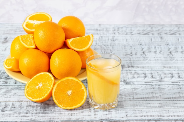 Vaso de jugo de naranja y un plato con naranjas sobre una mesa de madera