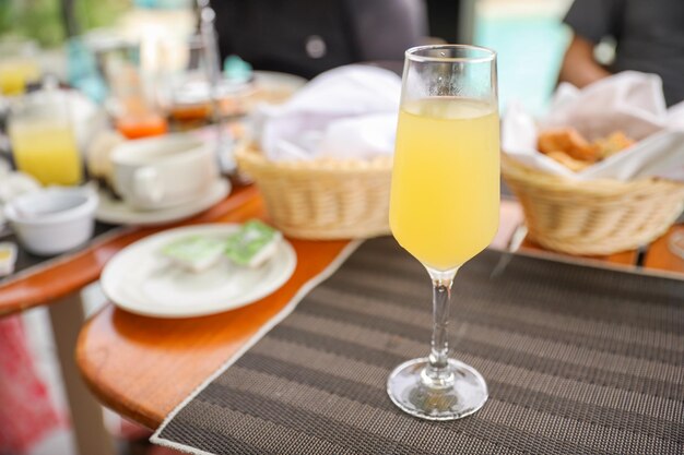 Un vaso de jugo de naranja se sienta en una mesa con una canasta de pan y un plato de brunch.