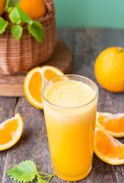 Un vaso de jugo recién exprimido rodeado de naranjas y mandarinas frescas. Foto vertical.