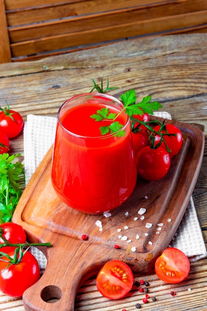 Vaso de jugo de tomate fresco de cerca en el tablero sobre la mesa.